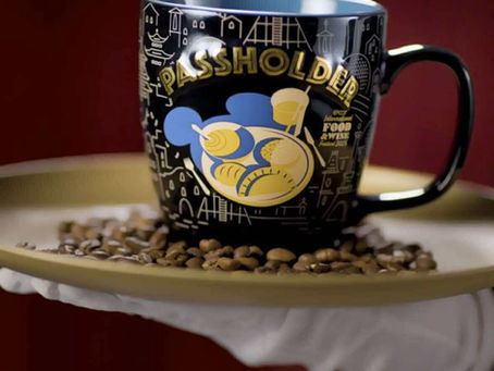 A mug with "Passholder" text sits on a gold tray with coffee beans. Dark background, elegant presentation, and intricate design.