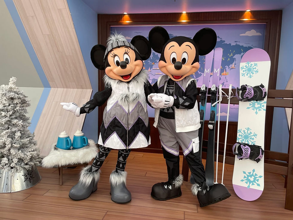 Mickey and Minnie in winter outfits, posing with skis and a snowboard indoors. A snowy tree and mugs of cocoa are nearby. Cozy atmosphere.