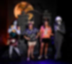 Two women pose with Sally and Jack Skellington costumes, wearing themed shirts and ears, in front of a Halloween backdrop with a moon.