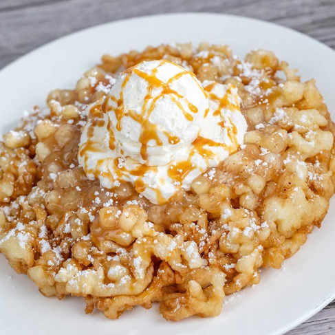 Funnel cake topped with vanilla ice cream and caramel drizzle on a white plate, wooden table background. Light, sweet, and indulgent.