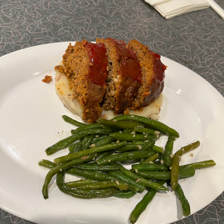 Homemade meatloaf on top of a serving of mashed potatoes with a side of fresh green beans