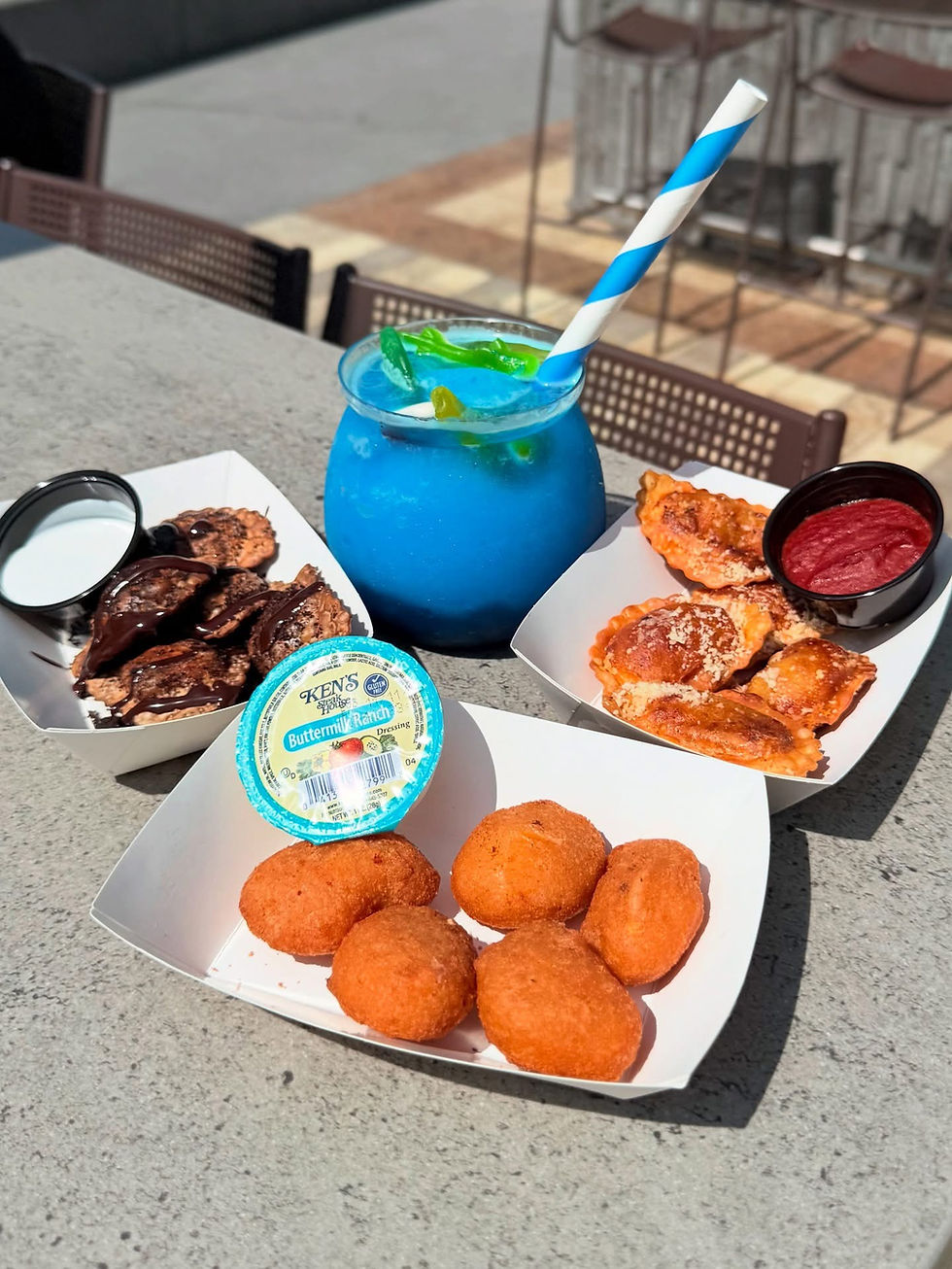 Blue slush drink with a straw, fried snacks in trays, and dipping sauces on a concrete surface. Bright, sunny outdoor setting.