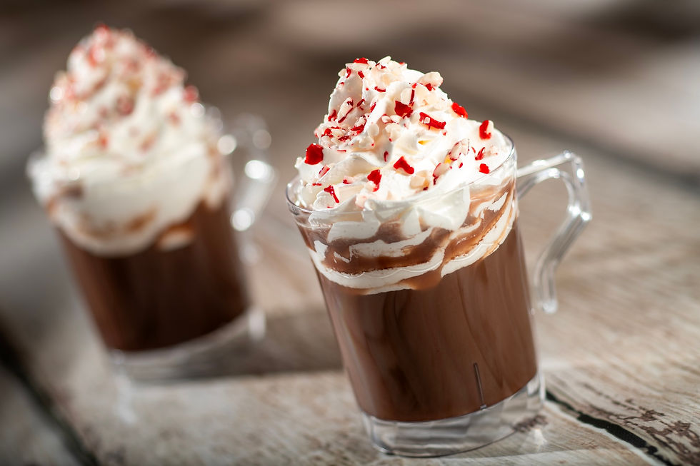 Two glass mugs of hot chocolate topped with whipped cream and red sprinkles on a rustic wooden table, creating a cozy, indulgent feel.