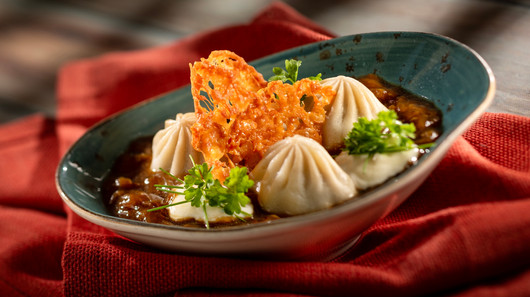 Dumplings with crispy garnish and parsley in a teal bowl on a red napkin. Warm, appetizing setting with rich colors and textures.