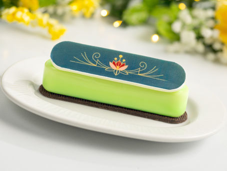 Green dessert on a white plate with a decorative blue topper featuring a red and gold floral design. Bright floral background.