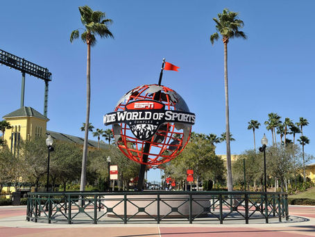 Red and silver globe with "ESPN Wide World of Sports Complex" text, surrounded by palm trees and clear blue sky, evokes excitement.