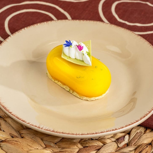 Yellow cake with cream and flowers on a beige plate. Background has a red cloth with white circles and woven material, creating a cozy feel.