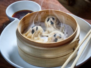 Steaming bamboo basket with panda-shaped dumplings, soy sauce in a dish, and chopsticks on a white plate. Warm wooden table setting.