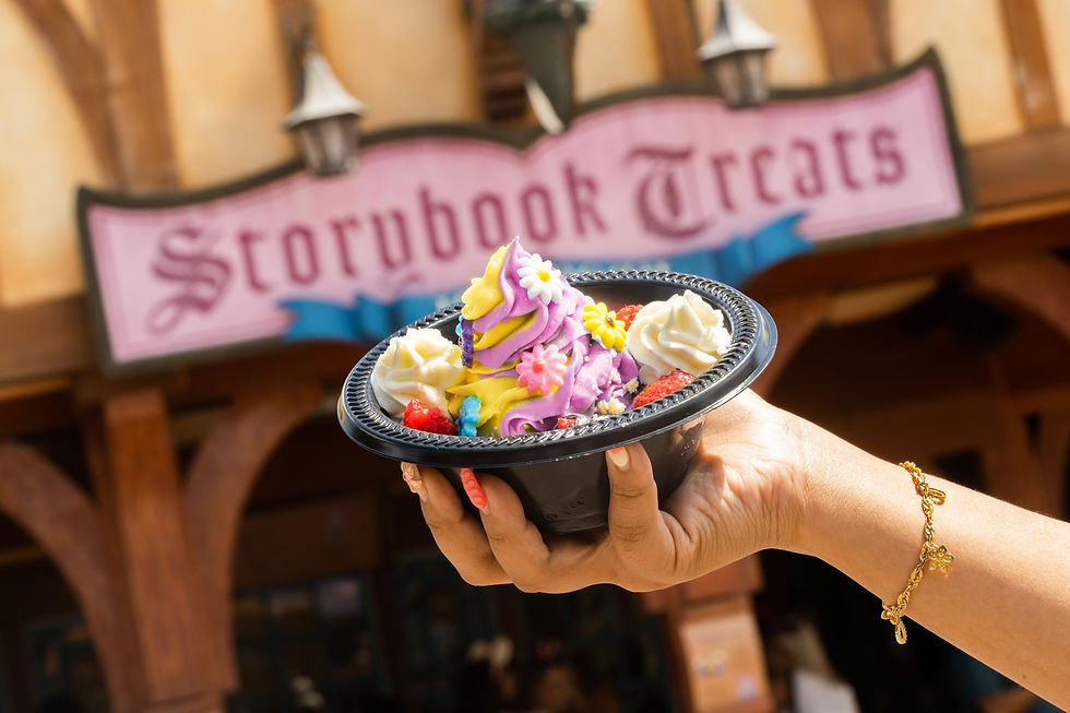 A hand holds a colorful dessert with flowers in front of the Storybook Treats sign. Bright, cheerful, fairytale-themed setting.