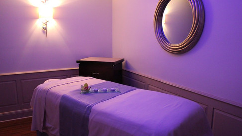 Massage room with a bed covered in white and purple linens, lit by soft wall lights. A round mirror reflects the calm ambiance perfect for relaxing on a non-park day at Walt Disney World.  This spa room is at Disney's Grand Floridian.