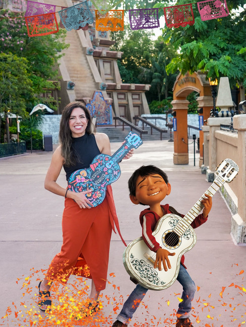 Woman and animated child with guitars, smiling in front of a temple with vibrant paper flags. Orange leaves swirl around their feet.