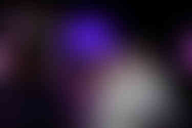 Three people smile under a glowing dome at night, with a neon heart above. They hold a lit wand. Background is vibrant with purple lights.