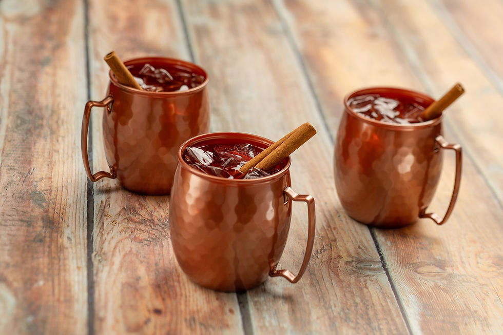 Three copper mugs with iced drinks and cinnamon sticks on a wooden table, creating a warm and inviting atmosphere.