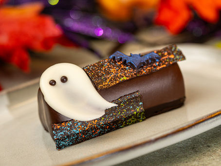 Chocolate dessert with white ghost and bat decorations on a speckled background. Leafy autumn colors and purple accents in the background.