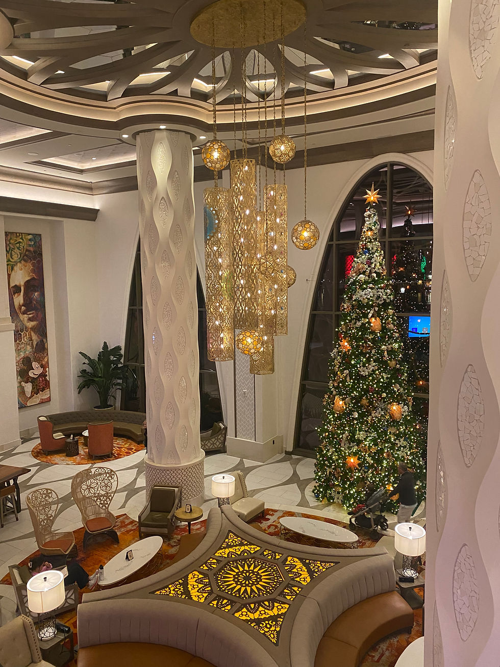 Luxurious hotel lobby with grand chandelier, intricate ceiling patterns, festive Christmas tree, and elegant seating areas creating a cozy ambiance.