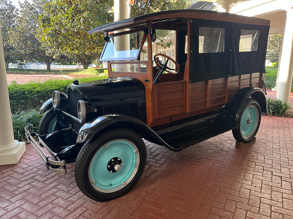 An antique green car with wood paneling sitting outside on a red brick drive. The overall photo displays summery warm tones with green trees and bushes in the background.