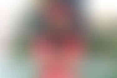 Woman in red shirt and Minnie Mouse ears blows sparkles from hands. Christmas tree with colorful ornaments in background. Festive mood.