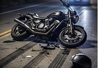 Cinematic twilight shot of a damaged motorcycle lying on its side on dark asphalt, next to a helmet and skid marks, with blurred police and emergency car headlights in the background.