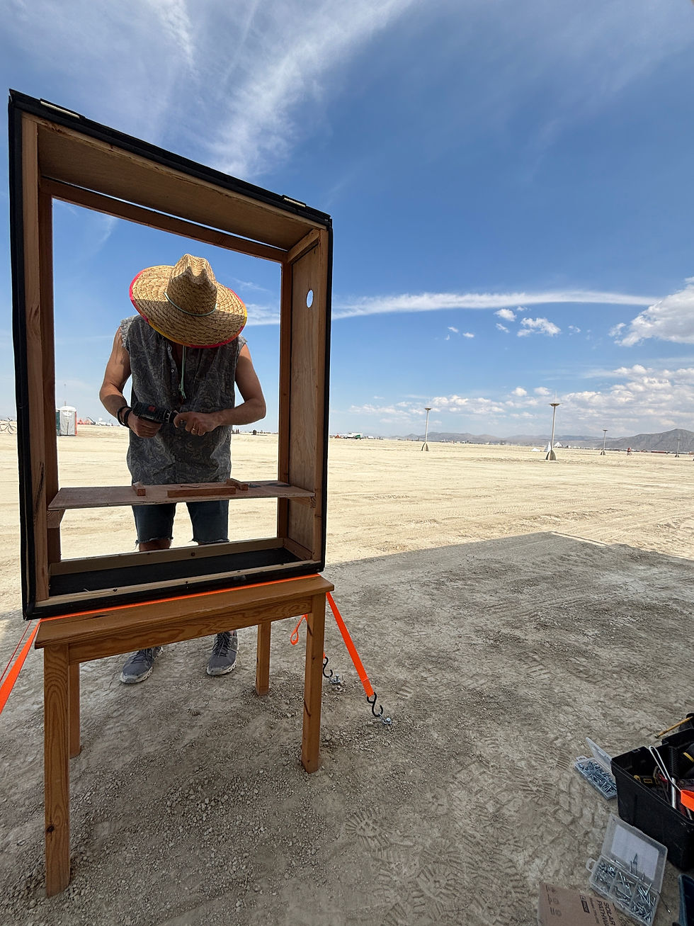A person in a straw hat assembles a wooden frame with tools in a desert setting under a blue sky. Bright orange straps are visible.
