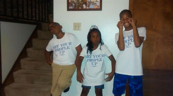 Three children wearing shirts that say Get Your People Up, posing together.