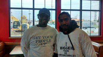 Two men smiling indoors, wearing shirts with text,
