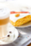 Stück Möhrenkuchen mit einem verschwommenen Latte Macchiato im Vordergrund