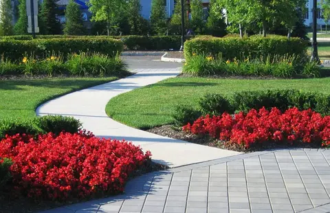 Winding concrete path through vibrant green lawn, red flowers, and hedges. | Down To Earth Landscaping | Jackson New Jersey, USA (732) 833-7702