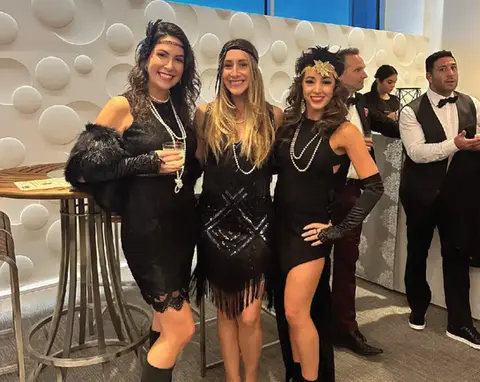 Three women in 1920s flapper attire smile at an event
