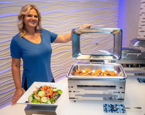 Smiling woman next to buffet with salad and hot food. | The Cambridge Club | Social Club of Aberdeen, NJ 07747