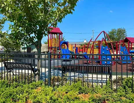Public playground with colorful playground equipment seen behind a black fence with two benches. Public commercial project services near me near me| Down To Earth Landscaping | Jackson New Jersey, USA (732) 833-7702