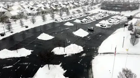 Aerial view of snowy parking lot with snow piles and cars.