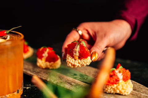 Hand reaching for a small appetizer with red topping | Violettes Woodbridge, NJ