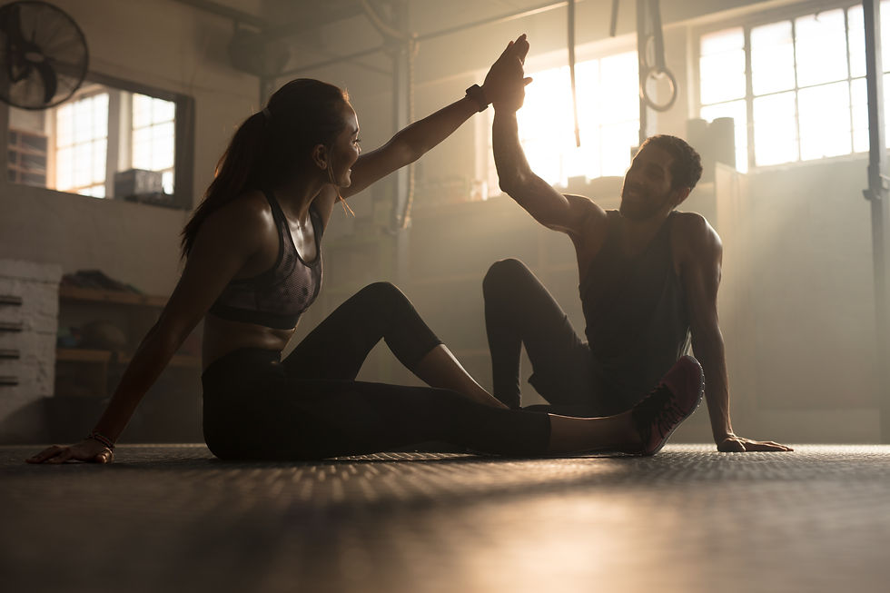 Healthy man and woman sitting on floor and giving each other high five at the gym. Fitness