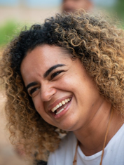 Liliane Xingú, mulher negra, cabelos crespos tingidos de loiro, veste blusa branca e sorri