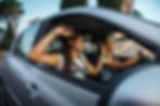 Two women laughing in a car together with the windows down on a sunny day.