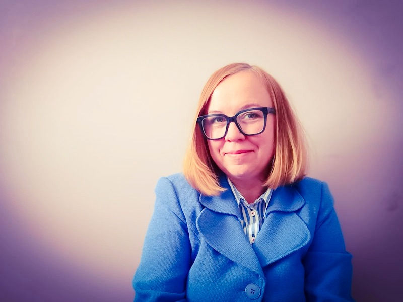 Woman with glasses and blue blazer smiling.