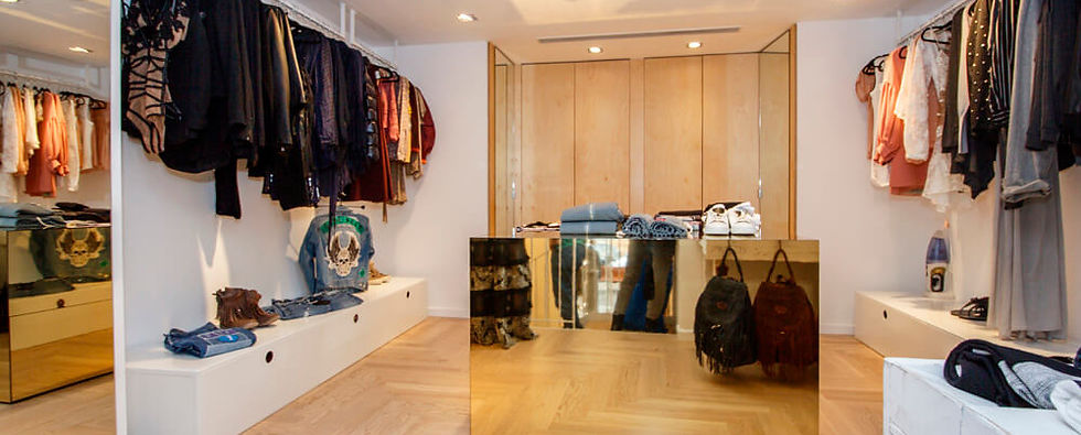 במרכזה של כיכר המדינה, אחד מאזורי האופנה היוקרתיים בתל אביב, נולד מחדש חלל מסחרי מרהיב. השיפוץ המקיף היה מסע משותף עם בעלות החנות, שחלמו על מרחב המשלב אלגנטיות עירונית עם נשמה ייחודית.
הקונספט העיצובי התבסס על ניגודים מרתקים - ברזל לבן נקי פוגש עץ טבעי חמים, כשביניהם מתנשא אי אחסון דרמטי העשוי כולו ממראות מוזהבות. האלמנטים הללו יוצרים דיאלוג מרתק של טקסטורות וחומרים, המשקף את הסגנון המתוחכם של לקוחות החנות. תכנון התאורה היה קריטי ביצירת האווירה הנכונה. שילבנו תאורה טכנית מדויקת להדגשת הבגדים עם תאורת אווירה רכה, היוצרת תחושה אינטימית ויוקרתית. מיקום המראות תוכנן בקפידה כדי להעצים את תחושת המרחב ולאפשר זוויות ראייה אופטימליות. אזורי התצוגה תוכננו כגלריה אופנתית, עם מערכות תלייה גמישות המאפשרות התאמה עונתית של החלל. חדרי ההלבשה עוצבו כמתחם אינטימי ומפנק, עם תאורה מחמיאה ואווירה המזמינה את הלקוחות להתנסות ולהתרשם מהפריטים בנינוחות מלאה.