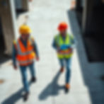 A high-angle, professional photograph of two construction professionals walking across a c