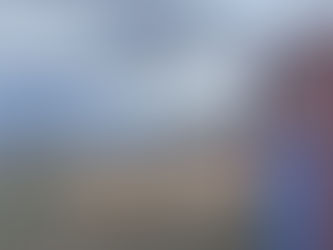 Bryn Kroto stands beside a shipping container in a field with buildings, shipping containers, and mountains in the background