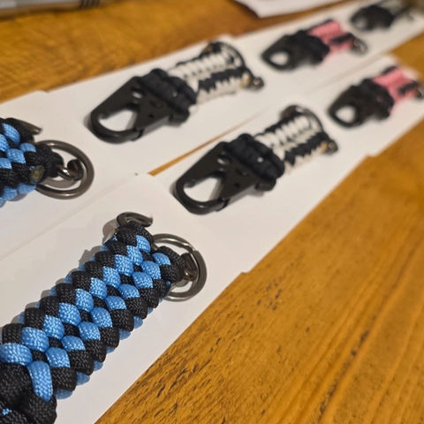 Several handmade cord keychains on white paper, various colors, on a wooden surface.