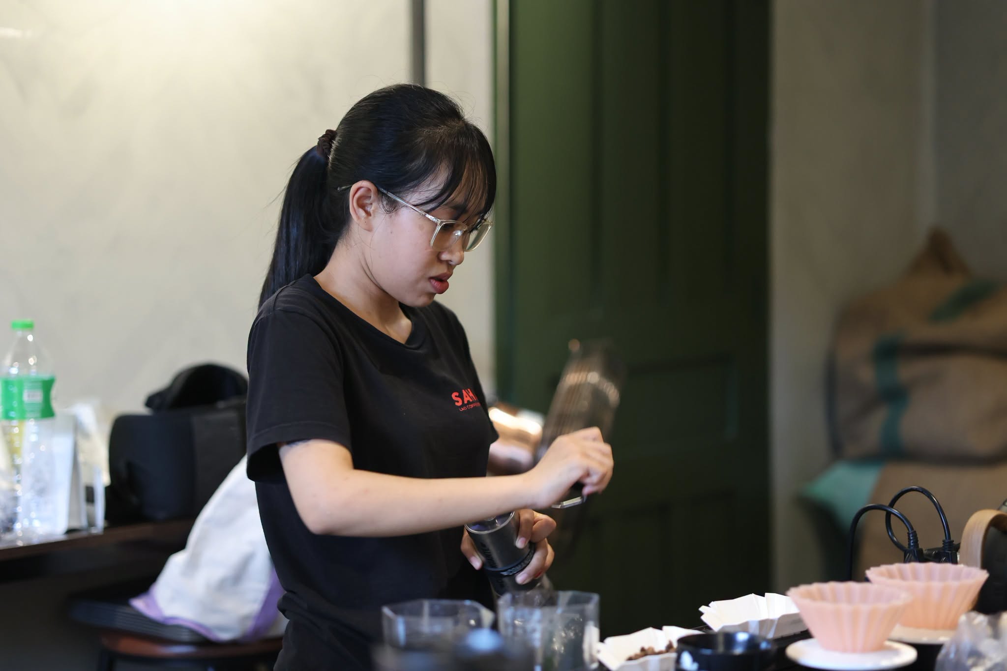 A learner using a hand grinder during Brewing Foundation practice at Sahai Lao Coffee Roastery in Luang Prabang.
