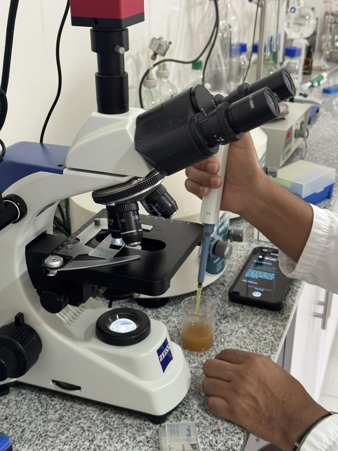 Original Colombia laboratory photograph showing a microscope beside a sample being handled with a pipette.