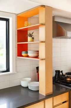 Plywood shelving with orange and red accents fits between a wall and post. 