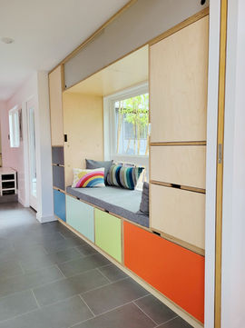 Built-in window nook with cushions, colorful storage drawers, and sliding doors in a modern, light-filled home.