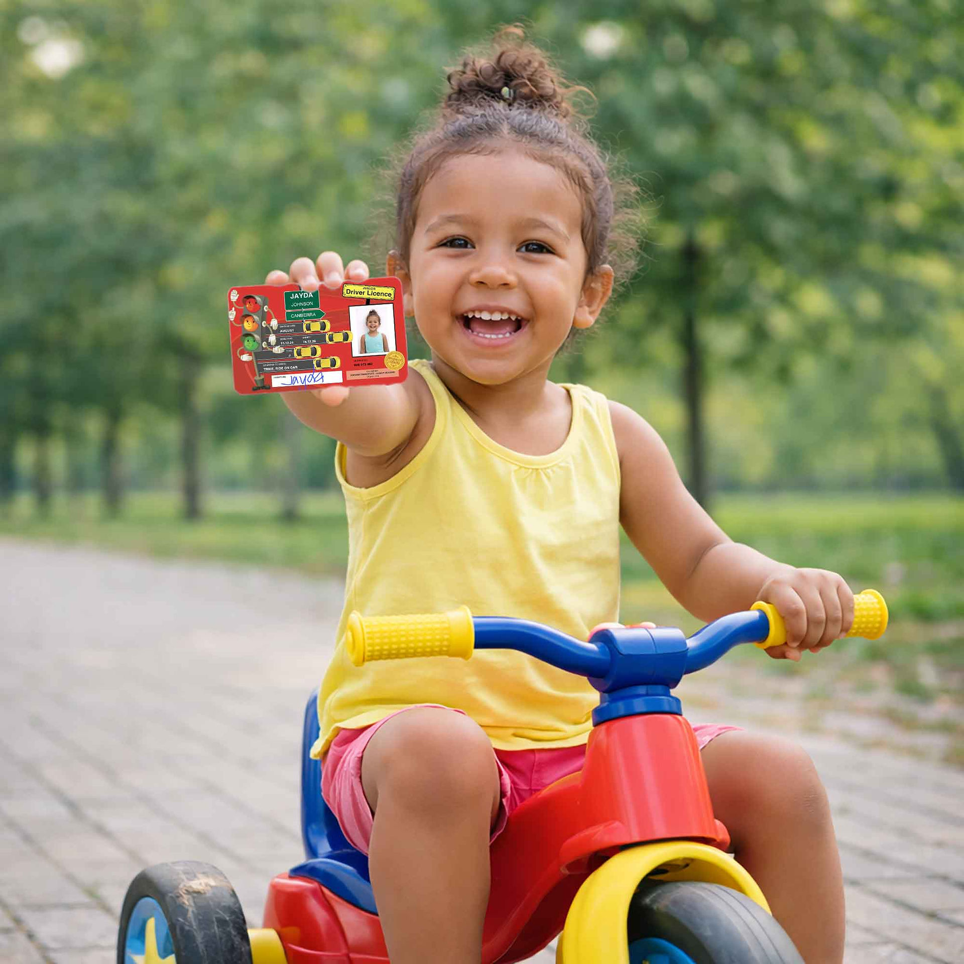 Young child riding a tricycle while proudly holding a junior driver licence