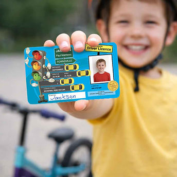 Smiling child holding a personalised ZiNGAMi junior driver licence card outdoors.