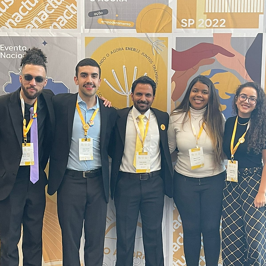 Na foto temos os membros que participaram do Eneb. São 5 pessoas, 2 universitários, 1 professor e duas universitárias, todas com roupas formais e o crachá do evento.