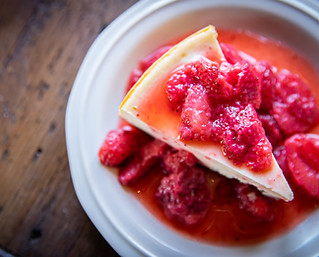 Stewarts' Cheesecakes Classic cheesecake slice on a white plate with strawberries in syrup on the top of the slice. The plate is on a wooden table and is offset to the right