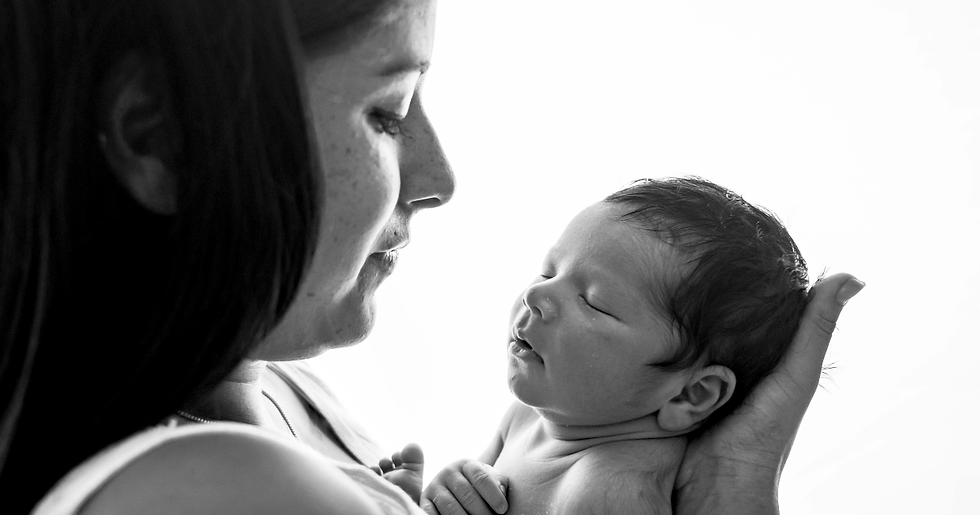 A woman lovingly cradles a sleeping newborn in her hands. The black and white image conveys tenderness and intimacy against a plain background.
