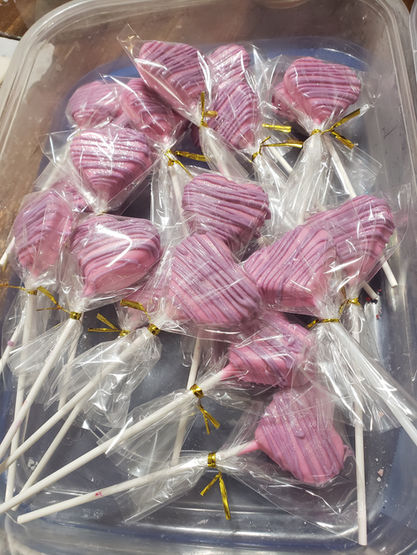Tray of individually wrapped pink cake pops with white drizzle.
